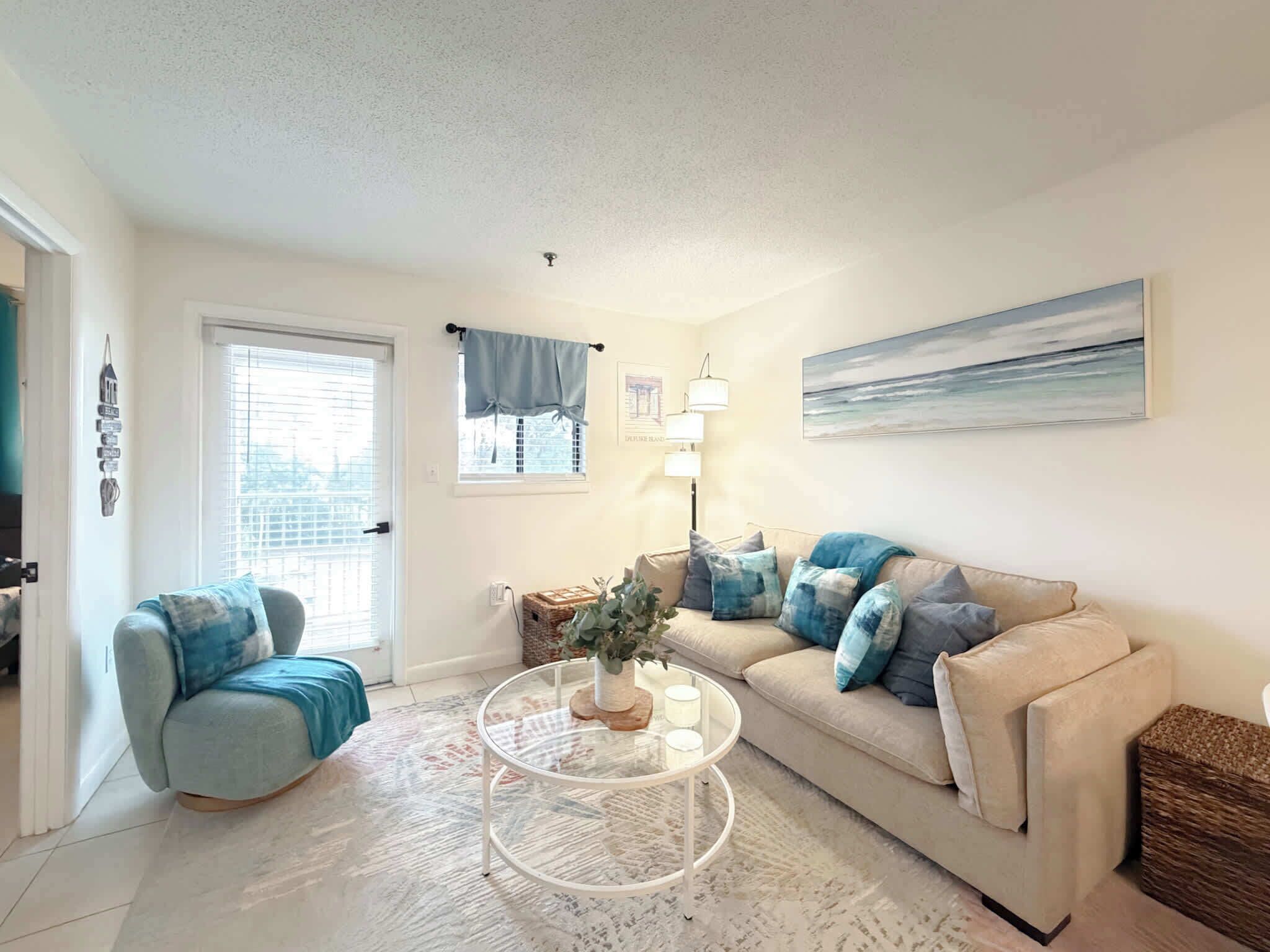A living room with a beige sofa, a round glass coffee table, and a blue and white patterned rug.