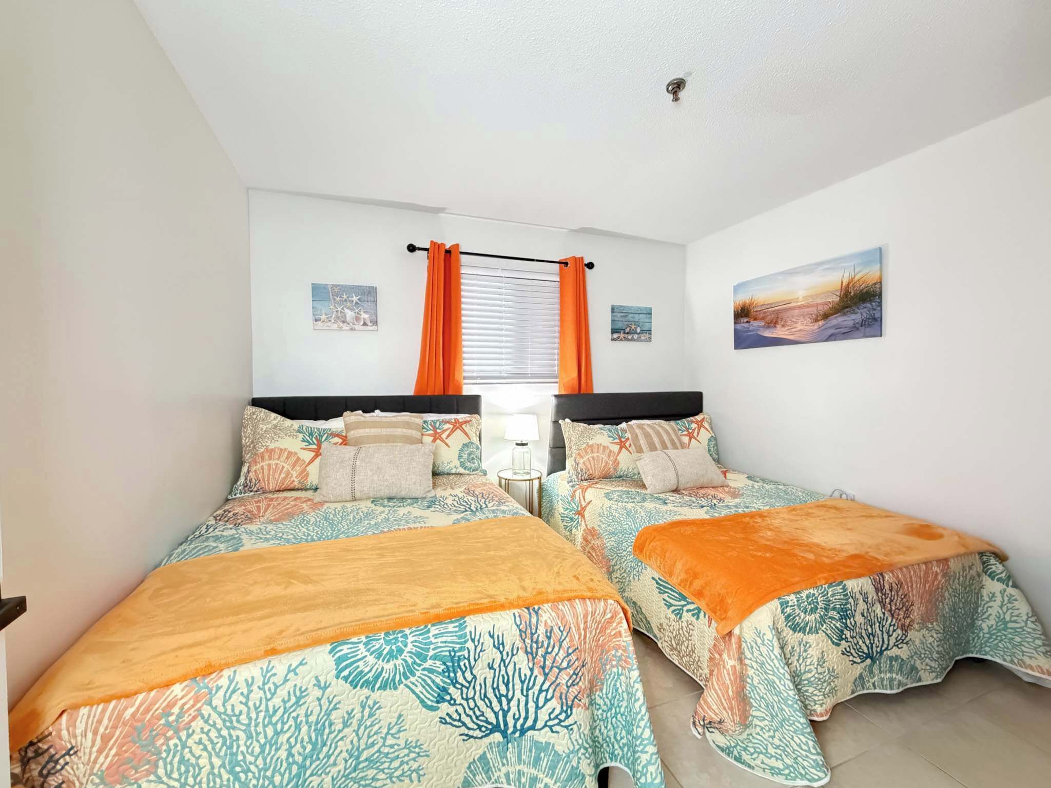 Une chambre avec deux lits, une fenêtre avec des rideaux et des œuvres d’art murales.