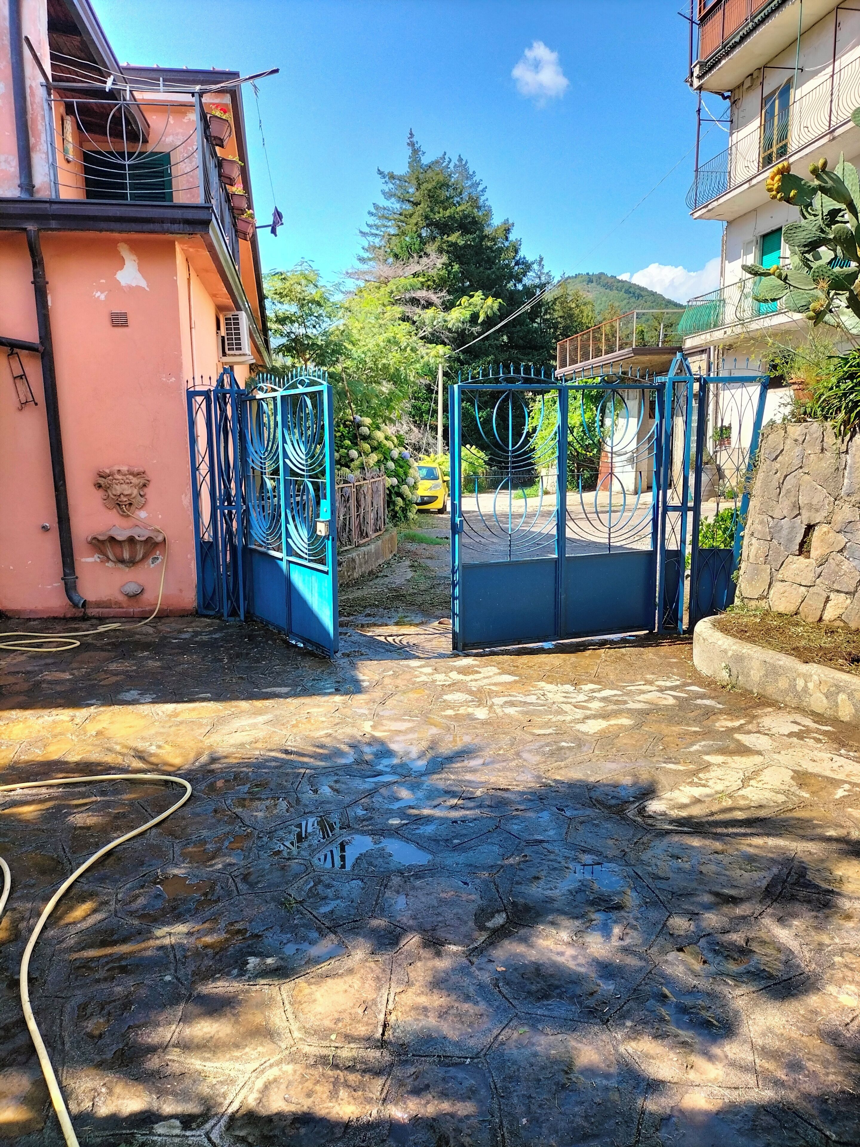Un cortile recintato con un ingresso lastricato, un edificio rosa e un cancello blu.