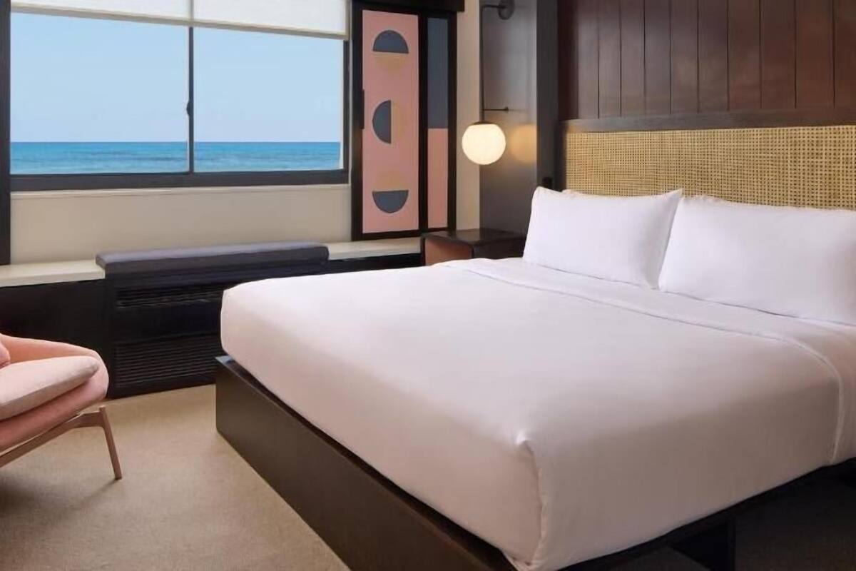 Une chambre d’hôtel avec un lit, une chaise, une fenêtre donnant sur la mer et une lampe fixée au mur.