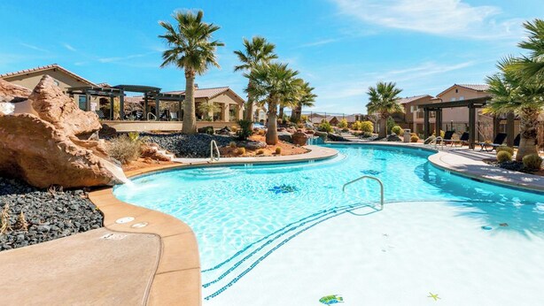 A swimming pool with a clear blue water, surrounded by palm trees and a rocky landscape. - 82-85 - Southern Cove Duplex in St George with Hot Tub (Santa Clara)