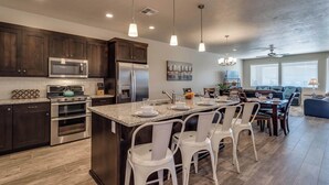 A modern kitchen with dark wood cabinets, stainless steel appliances, and a central island with white chairs. - 82-85 - Southern Cove Duplex in St George with Hot Tub (Santa Clara)