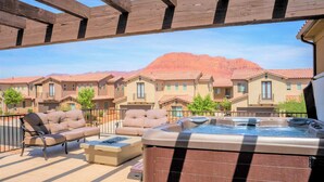 A patio with outdoor seating and a hot tub, overlooking a row of townhouses with a mountain in the background. - 82-85 - Southern Cove Duplex in St George with Hot Tub (Santa Clara)