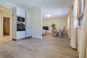 A modern kitchen with built-in appliances, a dining area with a table and chairs, and a small TV. - Leaf Apartment in Zurich Oerlikon (Zürich)