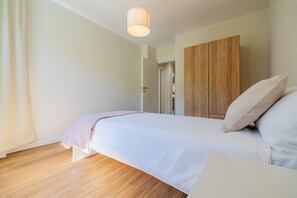 A bedroom with a bed, a wooden wardrobe, and a bedside table. - Leaf Apartment in Zurich Oerlikon (Zürich)