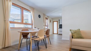 A modern living room with a sofa and a dining area with a table and chairs. - Leaf Apartment in Zurich Oerlikon (Zürich)
