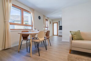 A modern living room with a sofa and a dining area with a table and chairs. - Leaf Apartment in Zurich Oerlikon (Zürich)