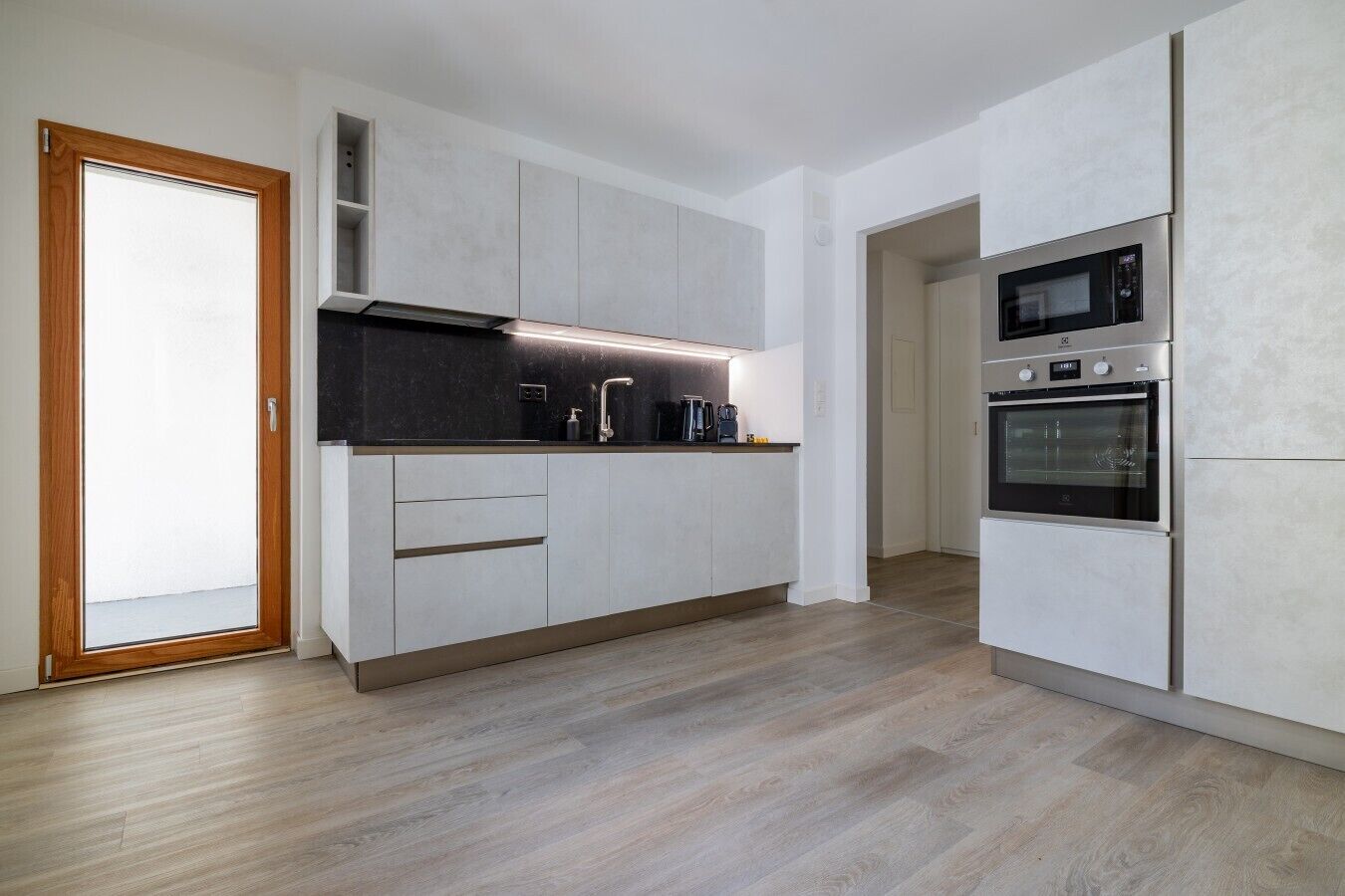 Une cuisine moderne avec des meubles blancs, un plan de travail noir et des appareils en acier inoxydable, notamment un four à micro-ondes et un four traditionnel.