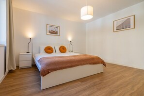 A bedroom with a bed, bedside tables, a lamp, a blanket, and two framed pictures on the wall.