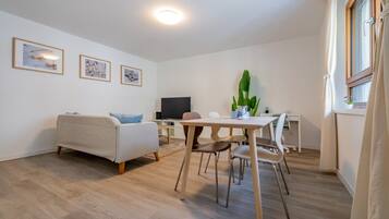Ein modernes Wohnzimmer mit einer Couch, einem Esstisch mit Stühlen, einem Flachbildfernseher und gerahmten Kunstwerken an der Wand.