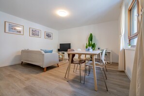 A modern living room with a sofa, a dining table with chairs, a flat-screen TV, and framed artwork on the wall. - Pure living Apartment in Zürich Oerlikon (Zürich)