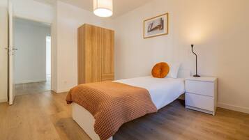 Ein Schlafzimmer mit Bett, Nachttisch, Lampe, Kleiderschrank und einer Tür zu einem anderen Raum.