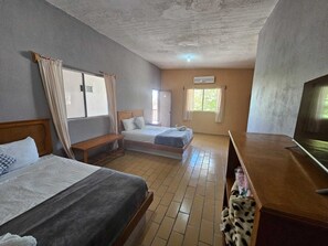 Una habitación de hotel con dos camas, un banco de madera, un televisor y una ventana con cortinas.