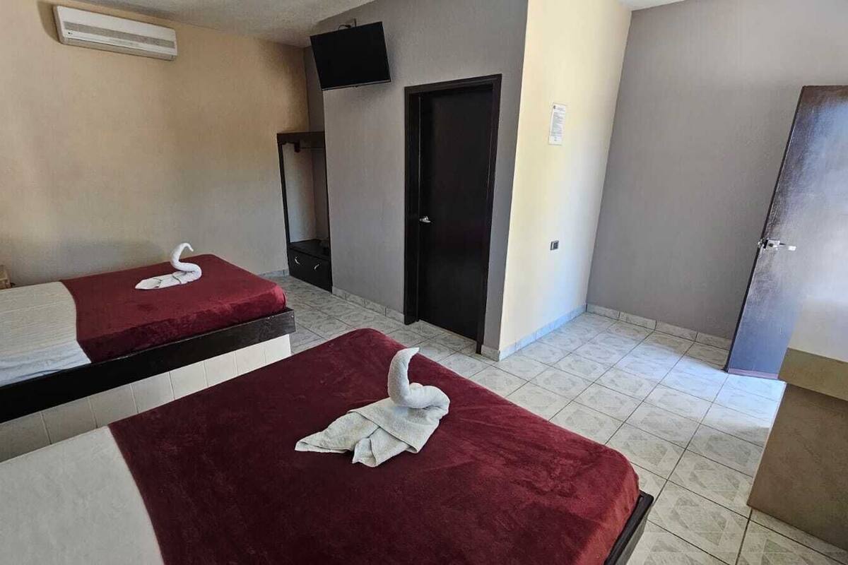 A hotel room with two beds, a TV, a door, and a small desk.