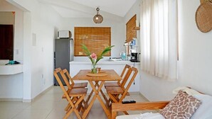 Un comedor con mesa y sillas de madera, un florero con flores, y una cocina al fondo.