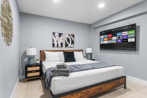 A modern bedroom with a bed, nightstands, a wall-mounted TV displaying streaming services, and abstract wall art. - Grand 8BR Oasis – Pool, Spa, Arcade Games (North Las Vegas)