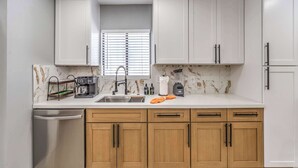 A kitchen with white cabinets, a stainless steel dishwasher, and a marble backsplash. - Grand 8BR Oasis – Pool, Spa, Arcade Games (North Las Vegas)