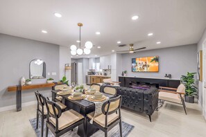 A modern dining area with a black dining table, beige cushioned chairs, and a chandelier.