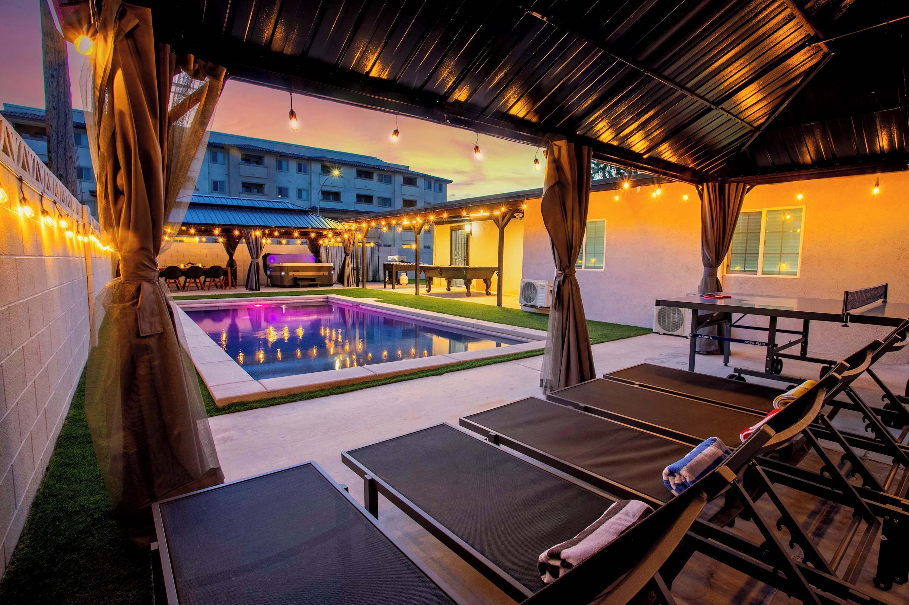 A poolside area with lounge chairs, a table, and string lights.