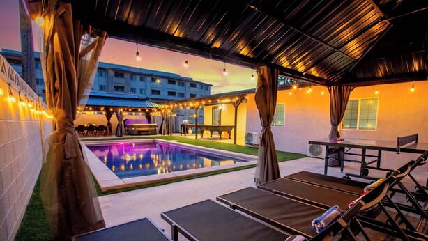 A poolside area with lounge chairs, a table, and string lights. - Grand 8BR Oasis – Pool, Spa, Arcade Games (North Las Vegas)
