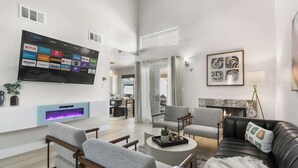 Uma sala de estar moderna com uma TV de tela plana na parede, lareira e um espaço de estar confortável com sofá e poltronas.