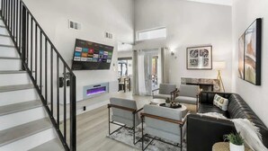 Uma sala de estar moderna com escada, televisão de tela plana e área de estar com sofá e poltronas.