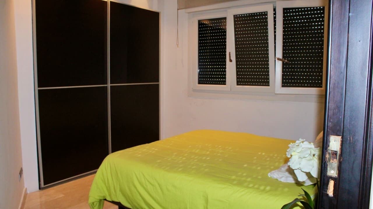 Ein Schlafzimmer mit Bett, Schrank und Fenster mit Rollläden.