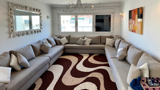 Ein modernes Wohnzimmer mit einer großen, L-förmigen Couchgarnitur, einem gemusterten Teppich und einer Kronleuchter.