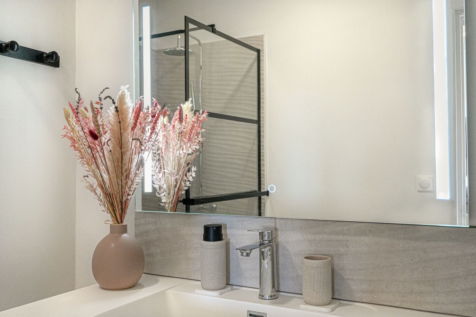 A bathroom with a white sink, a mirror, and a vase of dried flowers.