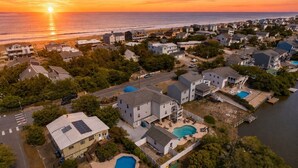 Zona residencial com casas, piscina e vista para o oceano ao pôr do sol.