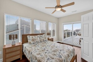 A bedroom with a bed, nightstands, a ceiling fan, and a view of a deck through a sliding glass door. - Luxe Sandbridge Beach, Waterfront, Pool, Arcade (Virginia Beach)