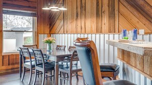 Un'area pranzo con tavolo e sedie in legno, una lampada a sospensione e vista sull'esterno.