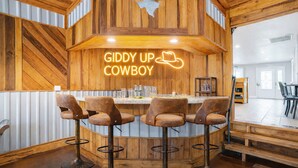 Un'area bar con pareti in legno, un neon con la scritta "GIDDY UP COWBOY" e tre sgabelli da bar.