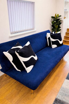Un canapé bleu agrémenté de coussins à motifs noirs et blancs, une plante en pot et un escalier en arrière-plan.