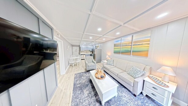 A modern living room with a sofa, coffee table, and TV. There is a dining area with chairs and a table. The room has a neutral color scheme and a large window with a painting. - FANTASTIC FIND! Great deals and in the heart of everything! Beaches, golf, shops (Hilton Head Island)