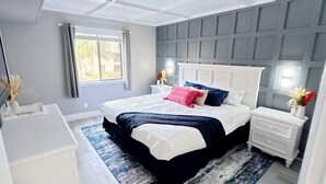 A bedroom with a large bed, white nightstands, a blue and white patterned rug, and a window with curtains. - FANTASTIC FIND! Great deals and in the heart of everything! Beaches, golf, shops (Hilton Head Island)