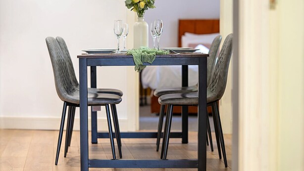 A dining table with four chairs, a vase with yellow flowers, and two wine glasses. - Luxury 2BR Apartment | Balcony | Free Parking | 5min to Docks | Sleeps 6 (Gloucester)