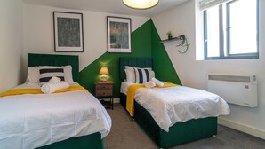 A hotel room with two beds, a green accent wall, a window with blinds, and a wall-mounted heater. - Luxury 2BR Apartment | Balcony | Free Parking | 5min to Docks | Sleeps 6 (Gloucester)
