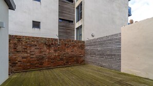 A courtyard with a brick wall, a wooden fence, and a concrete building. - Luxury 2BR Apartment | Balcony | Free Parking | 5min to Docks | Sleeps 6 (Gloucester)