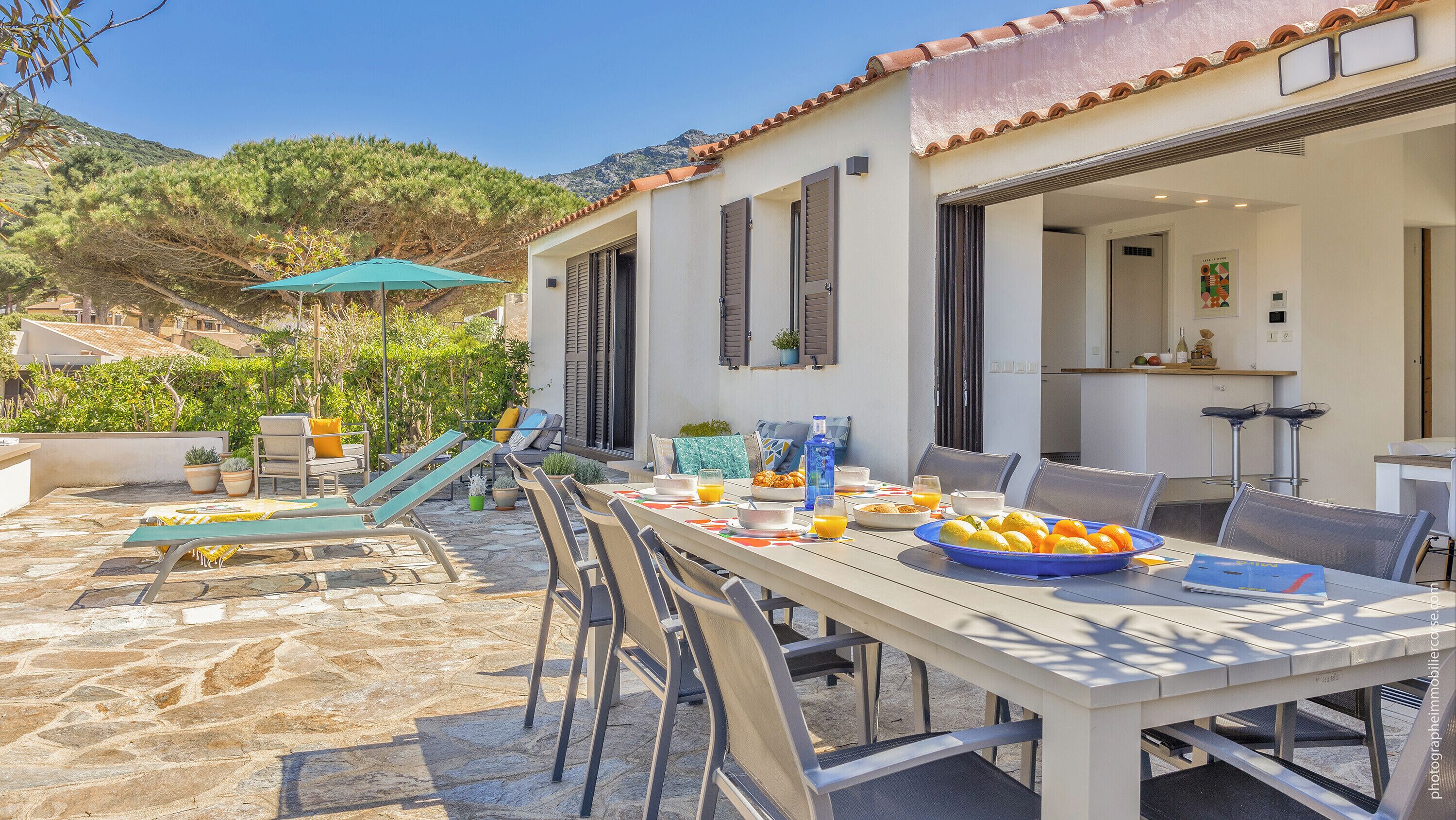 A dining area with a stone patio, outdoor seating, and a view of the surrounding landscape.