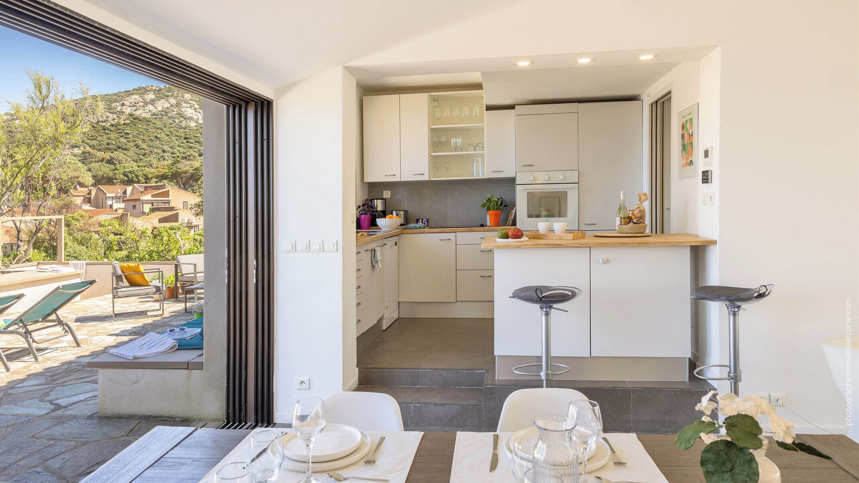 A modern kitchen with white cabinets, a wooden countertop, and a dining area with a table set for two.