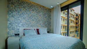 Une chambre d’hôtel avec un lit, une table de chevet, un mur décoré de motifs et une vue sur un immeuble par la fenêtre.