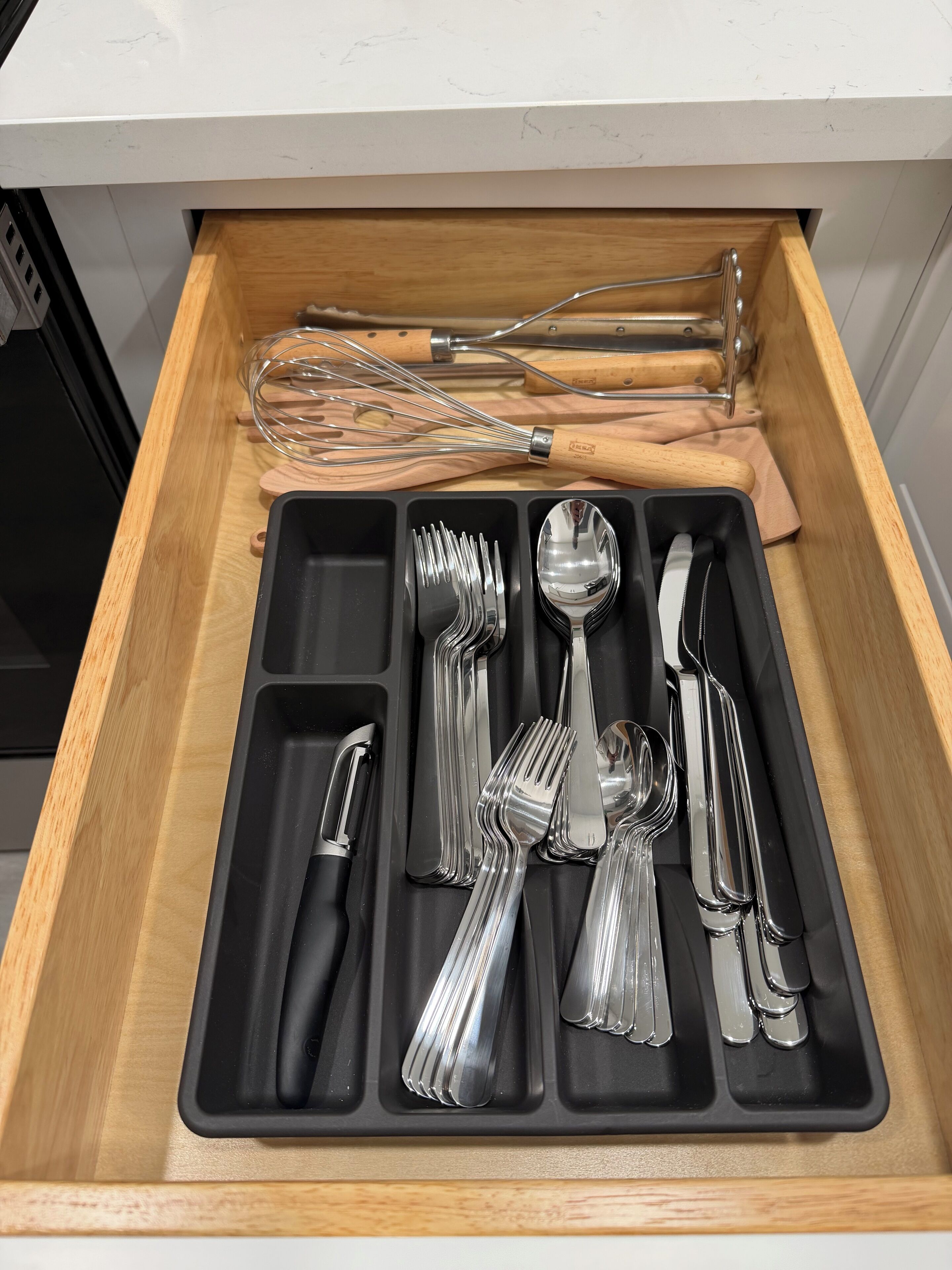 A drawer with a black tray containing various utensils, including forks, knives, and spoons.