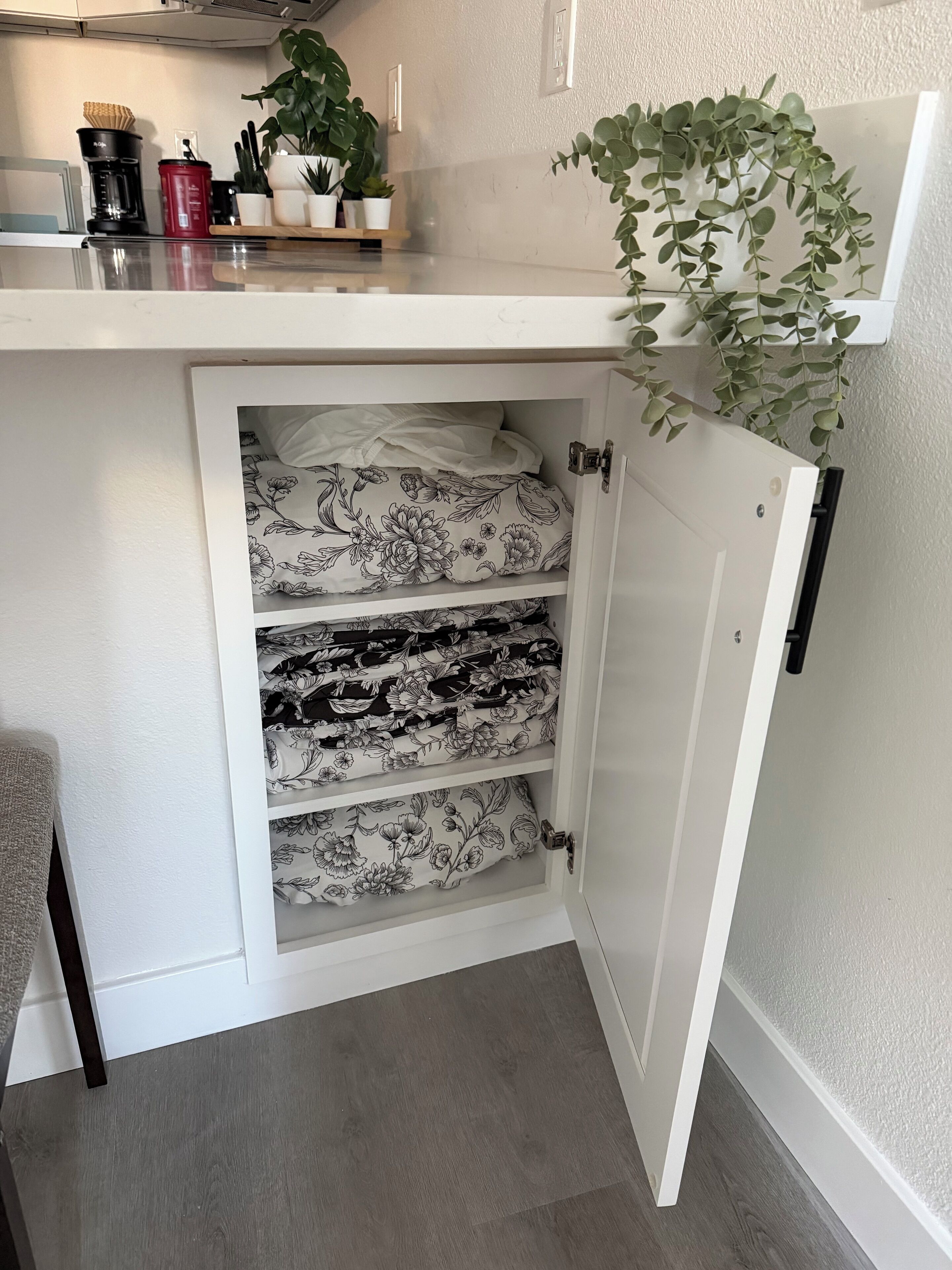 A white cabinet with floral-patterned bedding and a plant on top.