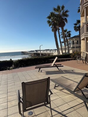 A beachside patio with lounge chairs, a pier in the background, and palm trees. - Casa de la Playa! (San Diego)