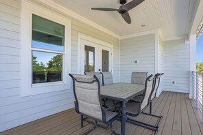 Une terrasse couverte avec une table et des chaises, un revêtement extérieur blanc et un ventilateur de plafond.