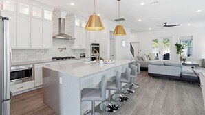 Una cocina moderna con armarios blancos, electrodomésticos de acero inoxidable y una isla central con taburetes de bar.