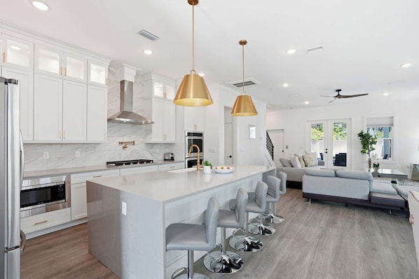 A modern kitchen with white cabinetry, stainless steel appliances, and a central island with bar stools.