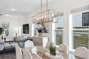 A modern living room with a dining area, large windows, and a chandelier.
