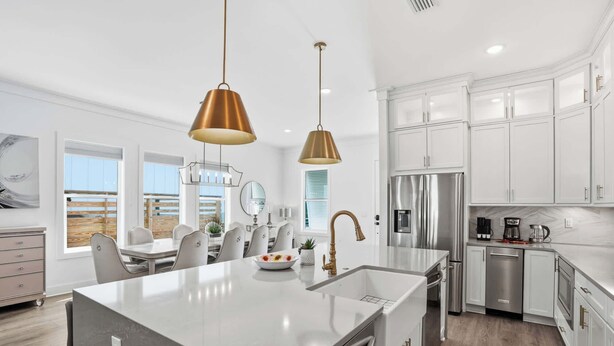 Una cocina moderna con muebles blancos, electrodomésticos de acero inoxidable y una isla central con un lavamanos y un jarrón de flores.